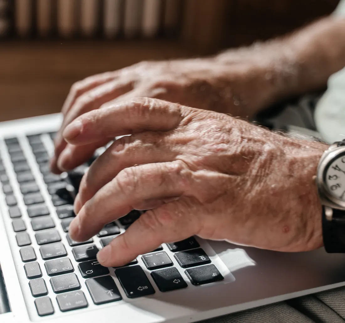 Manos de una persona mayor escribiendo en una laptop.