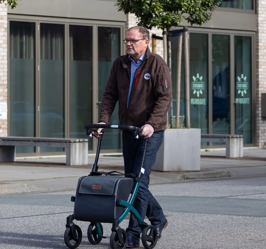 Un hombre mayor camina por la calle empujando un rollator.